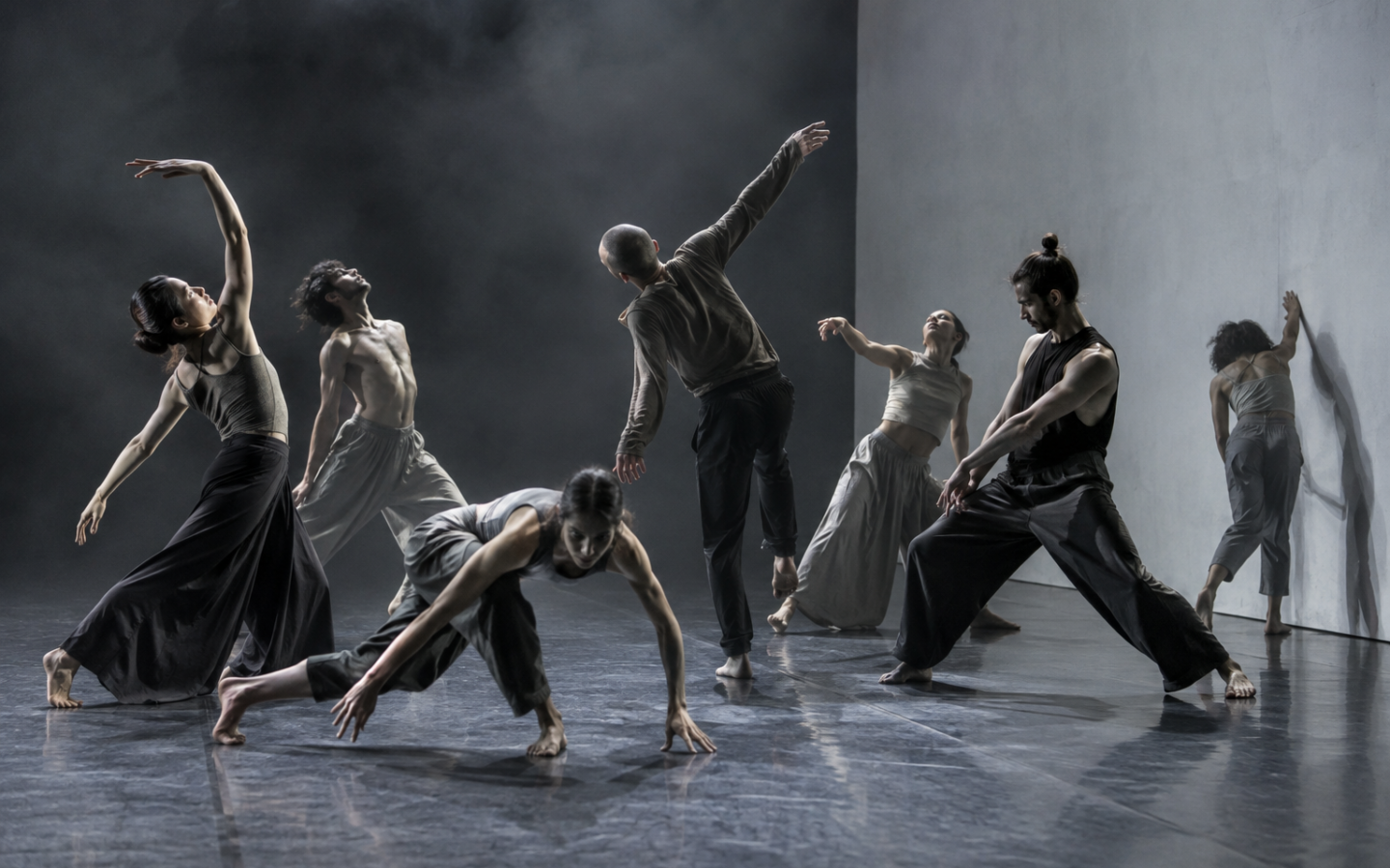 Ensamble de danza contemporánea en movimiento frente a un escenario gris minimalista